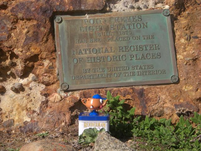 A small walking Pixar teapot at Point Reyes lighthouse, standing below the plaque explaining that Point Reyes is a historic place.